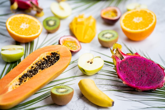 Frutti tropicali maturi e succosi di stagione. Papaya, kiwi, banana, mela, frutto del drago, foglie di palma su fondo bianco marmo. Vacanze, cibo sano, concetto estivo. Vista dall'alto.