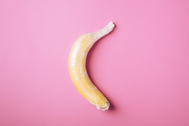 Frutto di banana avvolto in plastica elasticizzata su superficie rosa