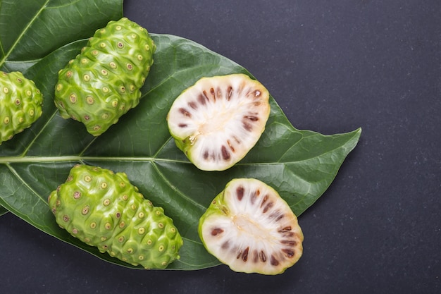 Frutto di Great morinda (Noni) o Morinda citrifolia albero e foglia verde su pietra nera