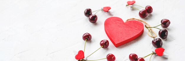 Frutto fresco stagionale di bacche di ciliegia rossa con vitamine sane su sfondo bianco e cuore rosso come simbolo d'amore della vacanza di San ValentinoL'amore è cura Ispirazione per San Valentino