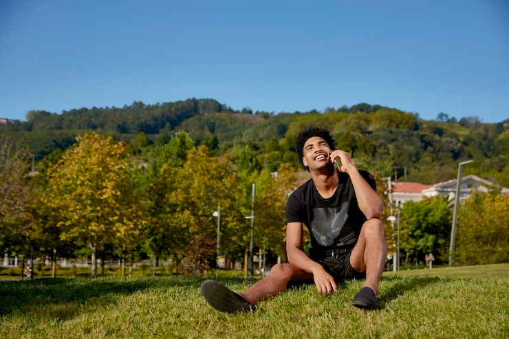 Photo full length of young man talking on phone sitting at park