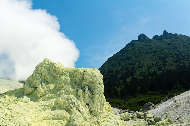 Fumarola fumante luminosa con depositi di zolfo sullo sfondo del picco del vulcano Mendeleev sull'isola di Kunashir