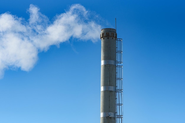 Fumo bianco dal tubo industriale sullo sfondo dell'inquinamento ambientale del cielo blu