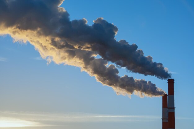 Fumo dai tubi industriali al tramonto contro un cielo blu