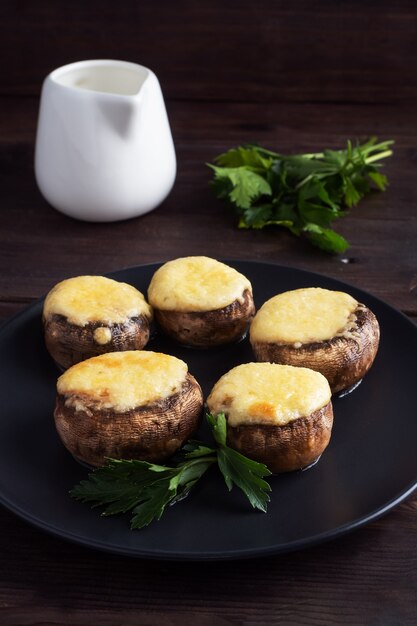 Funghi al forno ripieni di formaggio ed erbe su un piatto nero. tavolo di legno.