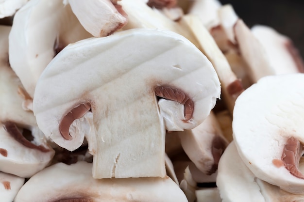 Funghi champignon affettati durante la cottura, primo piano di funghi tagliati per il trattamento termico