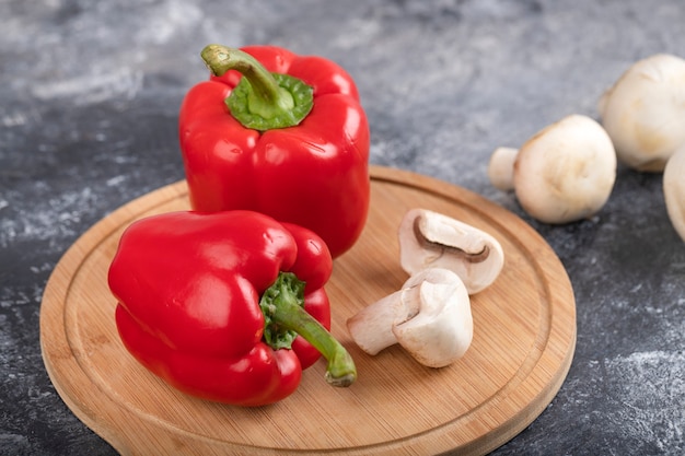 Funghi champignon crudi con peperoni rossi su tavola di legno.