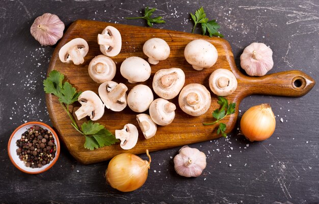 Funghi champignon freschi con verdure sul tavolo scuro, vista dall'alto