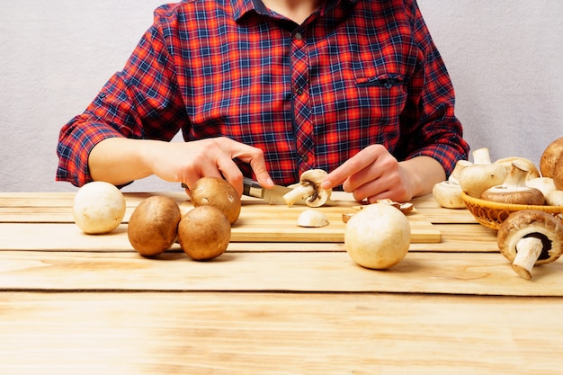 Funghi champignon freschi su una tavola di legno. La ragazza taglia i funghi con un coltello.