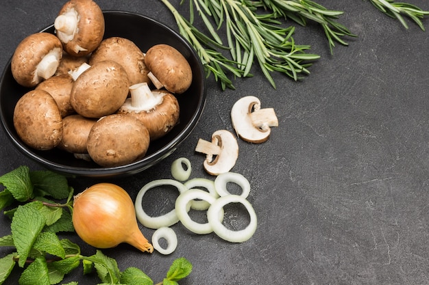 Funghi champignon in ciotola nera, cipolle tritate e funghi con rametti di menta e rosmarino