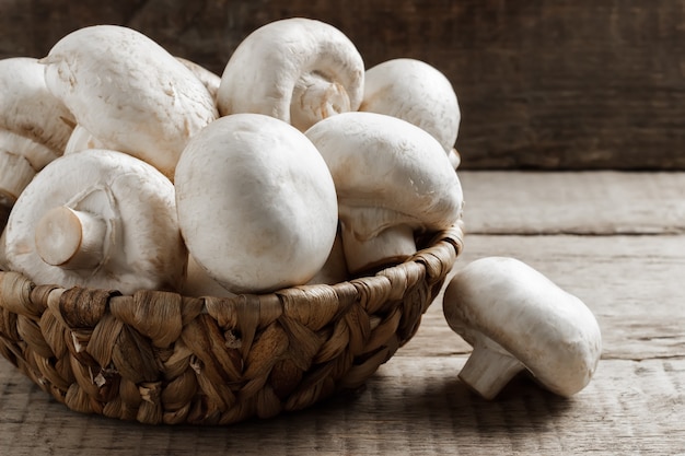 Funghi champignon in un cesto di vimini su uno sfondo di legno