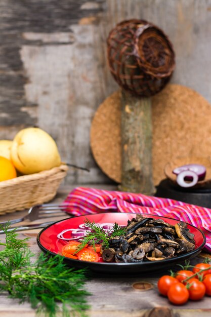 Funghi, cipolla e pomodori ciliegia fritti su un piatto su una tavola di legno