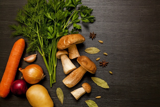 Funghi di bosco bianchi su fondo scuro con verdure, erbe aromatiche e spezie. Funghi freschi su un tavolo di legno.