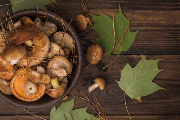 Funghi di bosco e foglie d'acero autunnali su un tavolo di legno. Cibo vegetariano naturale dalla foresta. Disposizione piatta.