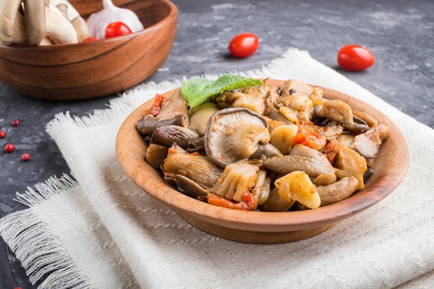 Funghi di ostrica fritti con i pomodori in zolla di legno sul nero