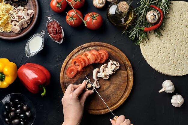 Funghi e pomodori tagliati a mano femminile su tavola di legno sul tavolo della cucina intorno a bugie ingredienti per p