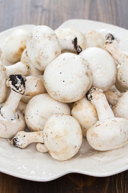 Funghi freschi in piatto bianco su superficie di legno