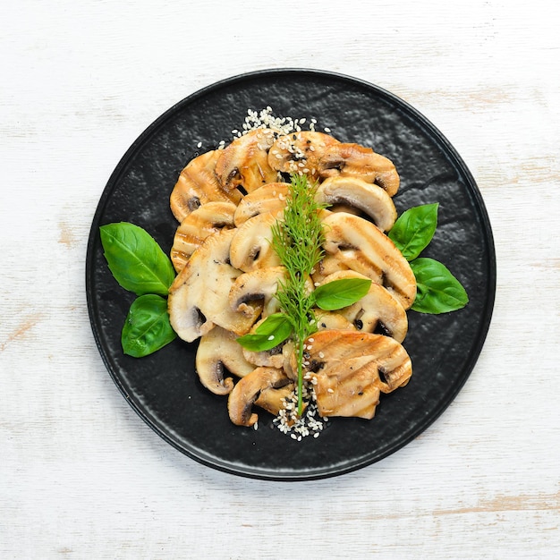 Funghi fritti con sesamo e basilico in un piatto nero su sfondo bianco di legno Vista dall'alto Spazio libero per il testo