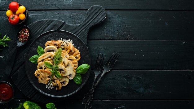 Funghi fritti con sesamo e basilico in un piatto nero su sfondo nero Vista dall'alto Spazio libero per il testo