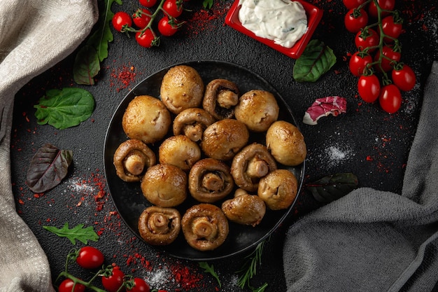 Funghi grigliati in un piatto scuro sul tavolo con spezie, verdure, erbe e cipolle