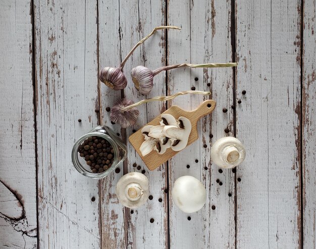 Funghi, pimento, aglio, un tagliere di legno, un barattolo di vetro con spezie su fondo di legno