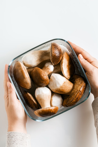 Funghi porcini grandi belli bianchi su bianco in una ciotola di vetro e mani femminili