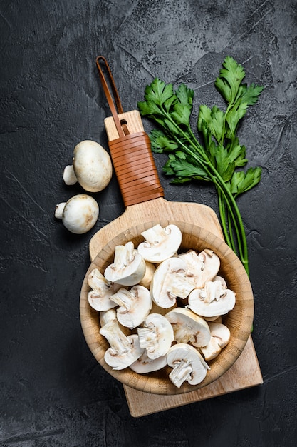 Funghi prataioli tritati in una ciotola di legno. Sfondo nero. Vista dall'alto