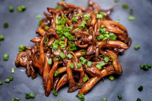 Funghi Shimeji serviti con erba cipollina su lastra di pietra nera. Pasto tipico orientale. Dettaglio del piatto di cibo, primo piano, messa a fuoco selettiva.