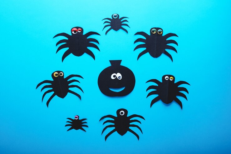 Photo funny paper spiders and pumpkin with eyes on a blue background. halloween decorations concept. happy halloween day. flat lay, top view. party invitation, celebration.