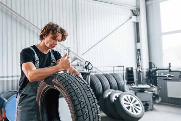 Funziona con pneumatici L'uomo adulto in uniforme di colore grigio è nel salone dell'automobile