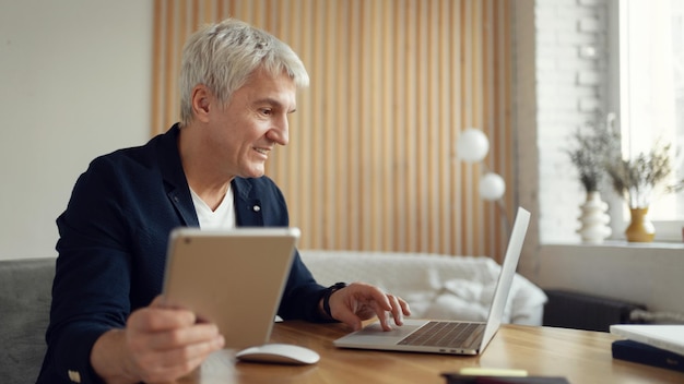 Funziona sorridendo su Internet su un sito online Un uomo di età elegante dai capelli grigi sul posto di lavoro