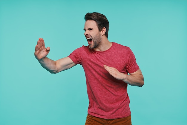 Furioso giovane uomo sorridente in abbigliamento casual gesticolando contro il muro blu