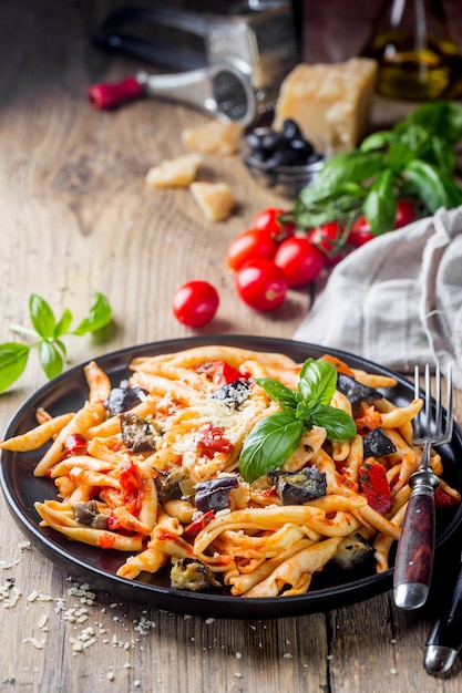 Fusilli al ferro con salsa di pomodoro, pomodori, melanzane, cipolla e pepe su un piatto.