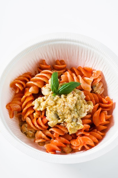 Fusilli al sugo di pomodoro con sugo di coniglio e basilico fresco in un contenitore di plastica da asporto