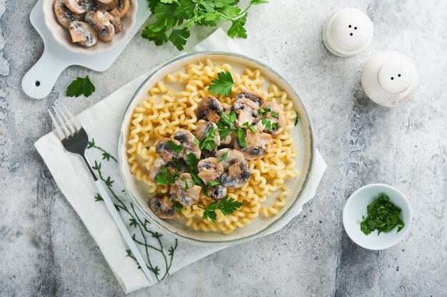 Fusilli con funghi, formaggio e salsa cremosa all'aglio su piastra su sfondo grigio di pietra o cemento Vista dall'alto Cucina tradizionale italiana