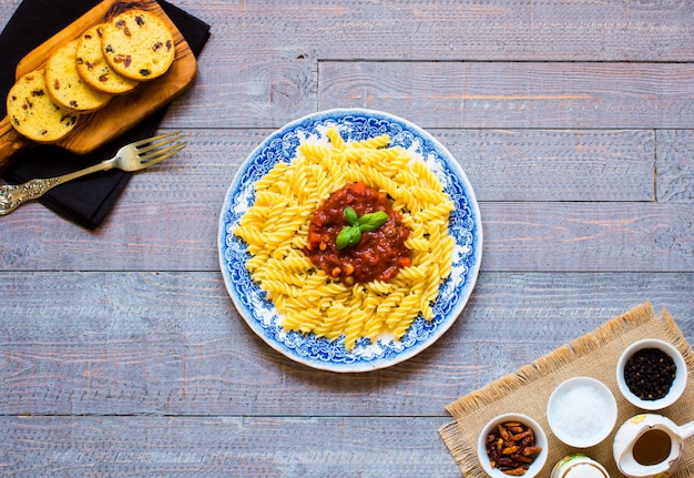 Fusilli con salsa di pomodoro, pomodori, cipolla, aglio, paprika secca, olive, pepe e olio d'oliva su un tavolo di legno