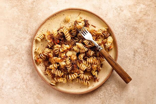 Fusilli con stufato di manzo su piastra e fondo beige Pasta Russian Navy Style Forchetta in legno