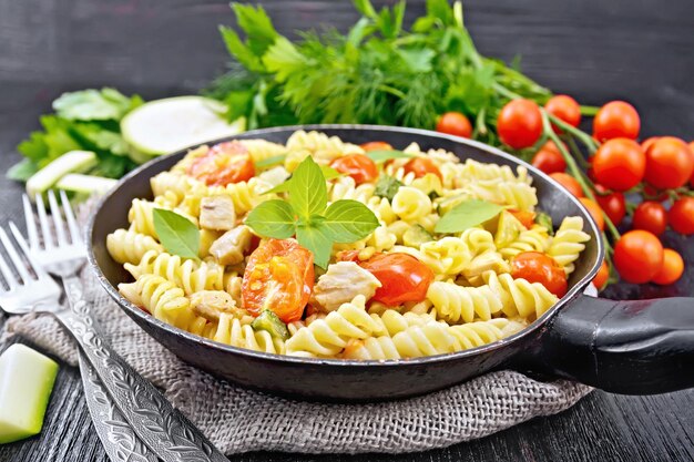 Fusilli con zucchine di pollo e pomodori in una padella su forchette di tela da imballaggio basilico e prezzemolo su fondo di legno scuro