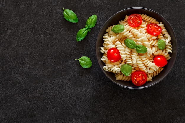 Fusilli cucinati con pomodori e foglia di basilico su sfondo scuro vista dall'alto spazio per copiare il testo