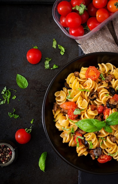 Fusilli di pasta con pomodori, manzo e basilico in ciotola nera sul tavolo.