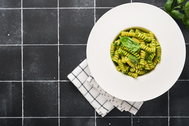 Fusilli italiani con pesto Fusilli con pesto di basilico ed erbe aromatiche parmigiano basilico e aglio su piatto bianco su sfondo di pietra nera Vista dall'alto Spazio di copia Mock up