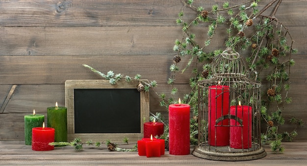 Gabbia per uccelli della decorazione di natale dell'annata, candele rosse e ramo di pino. interno nostalgico della casa con la lavagna su fondo di legno. immagine dai toni in stile retrò