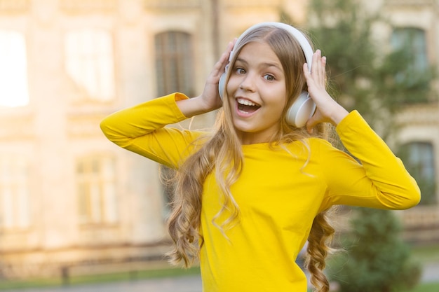 Gadget moderno di musica d'ascolto della ragazza. Bambino felice con auricolare senza fili all'aperto tramonto sfondo urbano. Cuffie stereo. Bambino che utilizza la tecnologia moderna. Bambino moderno. Canale musicale. Musica per l'anima.