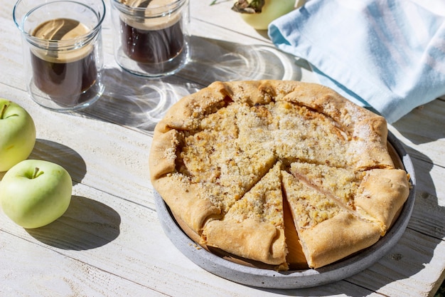 Galette di mele con streusel alla nocciola, servita con caffè su fondo di legno. Stile rustico.