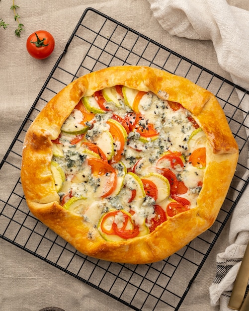 Galette salata fatta in casa con verdure, torta di grano con pomodorini, zucchine, gorgonzola. Crostata rustica in crosta su griglia su tovaglia di lino scuro.