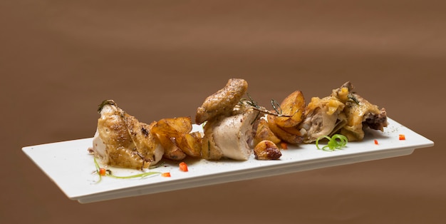 Gallo arrostito con patate, con erbe verdi, posto su un piatto bianco
