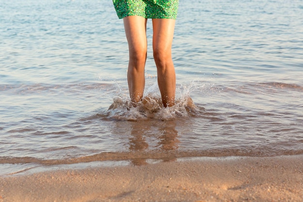 Gamba di donna che corre sulla spiaggia con spruzzi d'acqua vacanze estive gambe di una ragazza che cammina in acqua al tramonto