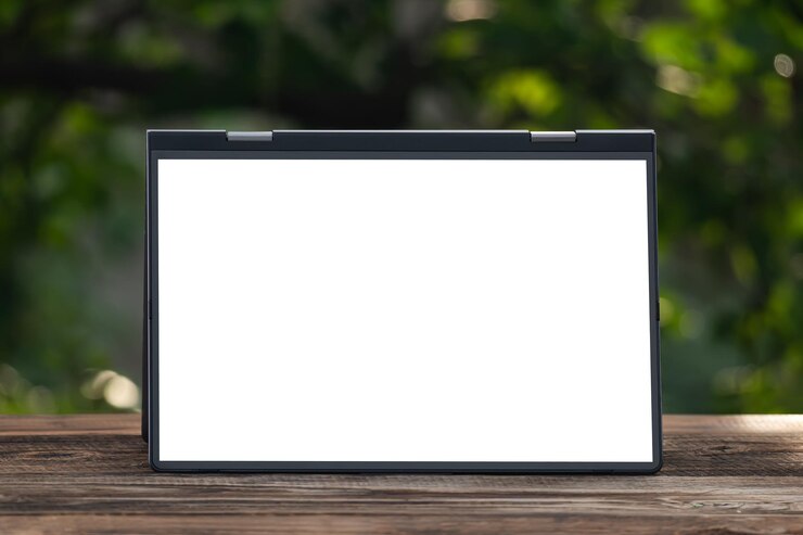 Photo gambar mockup laptop dengan layar putih kosong di atas meja kayu vintage di taman luar ruangan alami