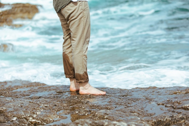 Gambe bagnate dell'uomo in pantaloni che camminano sulla spiaggia rocciosa del mare godendo le vacanze estive dell'acqua