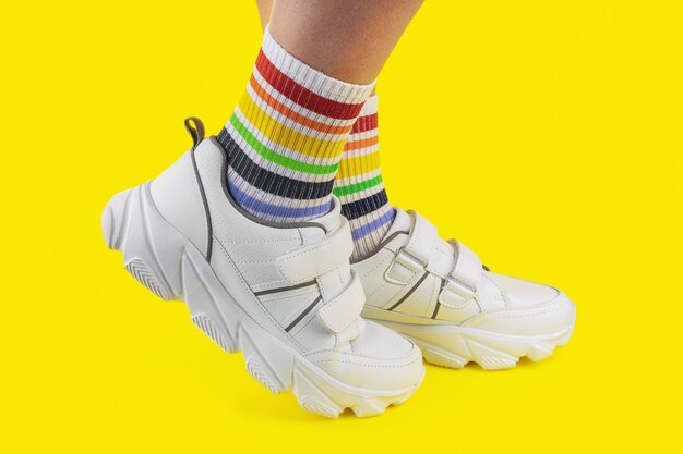 Gambe da donna in calzini multicolori a forma di arcobaleno con scarpe da ginnastica bianche su sfondo colorato, primo piano, lgbtq, orgoglio